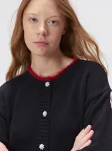 Cardigan de algodón grueso en color rojo, con cuello redondo y cierre frontal de botones grandes. Presenta bolsillos cuadrados en el bajo con detalles de pelo sintético en los bordes y logo bordado en uno de ellos. Posee puños y ruedo elastizados con diseño holgado.