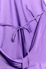 Vestido midi de satén color lila, con cuello halter y tirantes finos. Presenta un detalle de nudo en la cintura y espalda descubierta.