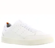 Zapatillas urbanas de caña baja, color blanco hueso, con suela gruesa de goma. Presentan detalles de perforaciones en el lateral y un pequeño tirador naranja en el talón.