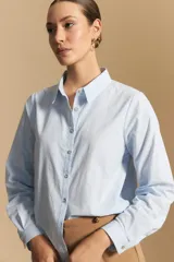 Camisa de corte clásico y holgado, confeccionada en tela blanca, con cuello camisero, cierre frontal de botones de nácar y mangas largas con puños abotonados.