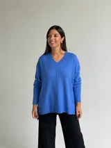 Sweater de tejido de punto color azul, con escote en V, manga larga con puños acanalados y diseño holgado con costura central vertical y ruedo asimétrico.