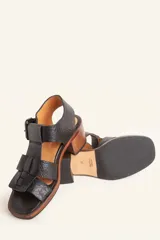 Sandalia de cuero vacuno texturado color negro, con tiras anchas y hebilla lateral. Taco ancho de madera.