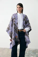 Ruana tejida de punto con diseño teñido artesanalmente en tonos lila y marrón, con terminación de flecos en el ruedo y etiqueta de cuero sintético en el frente.