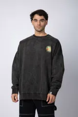 Buzo de cuello redondo y corte oversize, confeccionado en tela friza con efecto de teñido desgastado. Presenta una estampa pequeña en el pecho con diseño de sol y una etiqueta decorativa en el puño.