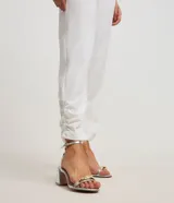 Pantalón de vestir blanco, modelo carrot, con cintura elástica en la espalda, cierre por cremallera y botón, detalle fruncido en el bajo y bolsillos laterales.