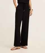 Pantalón femenino negro, modelo wide leg, de cintura alta con cordón ajustable y lazo. Presenta textura arrugada característica del tejido crepé airflow y bolsillos laterales.