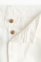 Jean de corte wide leg en denim de algodón rígido, con diseño de cinco bolsillos, cintura clásica con cierre de botones y piernas amplias.