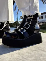 Botas cortas de cuero negro con plataforma y cuatro hebillas metálicas laterales.