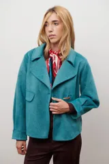 Chaqueta de paño color gris oscuro, con solapas amplias y cierre frontal mediante un alamar único. Presenta bolsillos laterales y mangas largas con puños rectos.