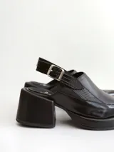 Zapato tipo slingback color negro, con plataforma y taco cuadrado. Presenta una puntera cuadrada y cierre con hebilla metálica en la tira trasera.
