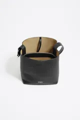 Bolso de hombro tipo cubo de estructura rígida, color marrón oscuro, confeccionado en piel vacuna. Posee asa regulable con hebilla metálica y cierre de cordón en la parte superior. Lleva el logo metálico de Bimba y Lola en la parte frontal inferior.