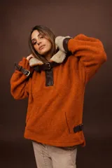 Buzo de tejido tipo lana color naranja con cuello de piel sintética, detalles en cuero marrón, correas ajustables con hebillas en cuello y mangas, y bolsillos laterales.