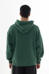 Buzo hoodie verde oscuro con estampa serigráfica frontal de alta definición con una escena urbana en estilo puntillista y logo VERNAL con efecto dorado envejecido. Corte oversize con hombros caídos, capucha doble y bolsillo canguro.
