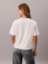 Remera boxy de algodón regenerativo en color blanco, con cuello redondo, manga corta y estampado gráfico con logo de Calvin Klein en el pecho.