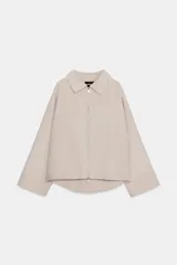 Chaqueta de lana en color beige, con cuello solapa, cierre frontal con cremallera metálica, mangas largas con corte evasé y bajo asimétrico.