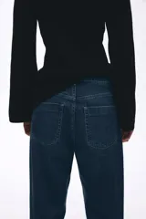 Jean de tiro alto con corte wide leg, confeccionado en denim rígido de lavado azul clásico. Presenta diseño de cinco bolsillos, cierre frontal con botón y ruedo desflecado.