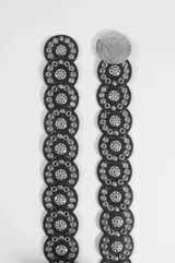 Cinturón ancho de cuero sintético negro, compuesto por piezas circulares unidas con detalles metálicos plateados en forma de ojales y apliques centrales, y hebilla circular grande plateada.