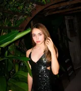Vestido midi de fiesta color fucsia con acabado brillante, compuesto por un top con escote en V y tirantes finos, y una falda con aberturas laterales en la cintura.