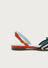 Sandalias planas destalonadas confeccionadas en rafia trenzada con patrón de zigzag en tonos azul marino y crudo. Tienen punta cerrada con una borla decorativa de flecos naranjas en el empeine, y una tira trasera ajustable de cuero naranja con hebilla metálica dorada.
