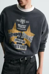 Sudadera de corte boxy fit en color gris oscuro con efecto lavado. Presenta cuello redondo en contraste color crema, manga larga con puños acanalados y estampado gráfico frontal con estrellas y tipografía estilo vintage.