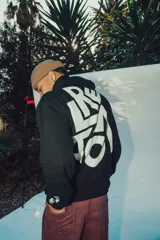 Hoodie negro con capucha, de corte holgado, que presenta un diseño gráfico grande en color blanco en la espalda y un detalle estampado en la manga.