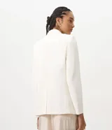 Blazer estructurado color blanco de la marca Cortelle, con solapa clásica, bolsillos frontales con solapa, mangas largas y cierre frontal de botones. Incluye un broche decorativo dorado con flecos de pedrería.