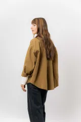 Sobrecamisa de gabardina liviana color crema, con corte oversize, cuello clásico, cierre frontal con botones a presión y dos bolsillos delanteros con solapa.