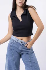 Top sin mangas de tejido acanalado, color negro, con cuello polo abierto y escote pronunciado en V. Presenta un pequeño parche con inscripción en el bajo.