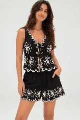 Conjunto de dos piezas negro con bordados florales en color crudo, compuesto por una musculosa de escote en V con lazos frontales y un short de cintura elástica.