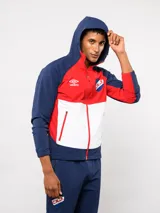 Campera deportiva Umbro del Club Nacional de Football, modelo Summit. Presenta un diseño con bloques de color en azul, rojo y blanco, con capucha, cierre frontal y bolsillos laterales con cierre. Incluye el logo de la marca y el escudo del club en el pecho.