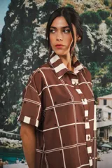 Vestido camisero corto marrón con estampado a cuadros blancos y bolsillo en el pecho.