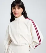 Campera deportiva color blanco hueso, con textura de malla waffle, cuello alto y cierre frontal. Presenta dos franjas verticales de color bordó en las mangas.