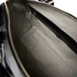 Cartera tipo baúl confeccionada en cuero negro con acabado brillante. Cuenta con dos manijas superiores, correa larga regulable y desmontable, detalles de cierres frontales verticales y herrajes metálicos plateados con el logo de la marca.