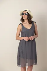 Vestido corto de seda color gris oscuro, con escote redondo y tirantes anudados en los hombros. El calce es suelto y la tela es ligeramente transparente.