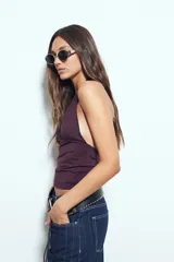 Top halter negro de silueta ajustada y diseño cropped, con escote profundo en V y frunce bajo el busto. Presenta espalda descubierta con lazo regulable en el cuello.