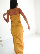 Top strapless color rojo vibrante, con frunces y pliegues que crean un efecto escultural y volumen en la parte delantera. Presenta un corte frontal con abertura central.