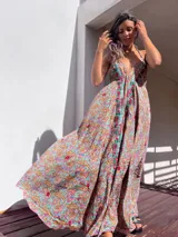 Vestido largo de estilo boho, con estampado tipo paisley en tonos tierra, turquesa y rosa. Presenta un escote profundo con tirantes finos y detalles de bordados florales en color rojo y verde a lo largo del frente.