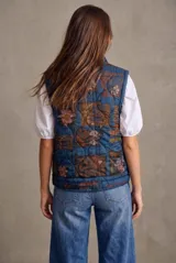 Chaleco acolchado de algodón en color azul lavado, con cierre frontal de cremallera y botones a presión, cuello alto y bolsillos frontales.