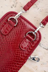Bandolera porta celular color rojo con textura croco, cierre de cremallera plateada y correa fina ajustable.