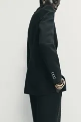 Blazer de corte estructurado con hombreras, cuello solapa y manga larga. Presenta un diseño cruzado con cierre frontal de botones y bolsillos delanteros con solapa.