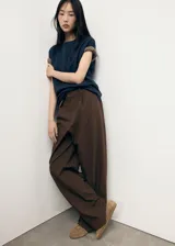 Pantalón de vestir marrón de tiro bajo y diseño wide leg, con pinzas frontales, trabillas para cinturón, bolsillos laterales y cierre oculto con botón, gancho y cremallera.
