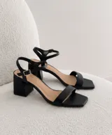 Sandalias negras de tacón bajo y ancho, con punta cuadrada, talón abierto y tira fina ajustable al tobillo.