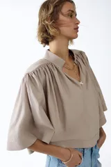 Blusa capa color beige con cuello alto, hombreras y diseño acampanado con frunces.
