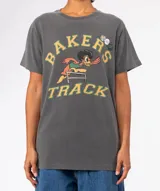 Remera de algodón gris oscuro con lavado especial, cuello redondo y manga corta. Estampado frontal con el texto "BAKER'S TRACK" y un personaje animado de pato saltando una valla.