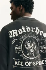 Buzo negro de algodón de peso medio con cuello redondo, hombros caídos y remates acanalados. Presenta un estampado frontal de una calavera rodeada de texto y texto en ambas mangas en tipografía gótica.