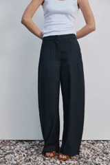 Pantalón de vestir de corte ancho y relajado, color negro con sutiles rayas diplomáticas verticales. Presenta bolsillos laterales y cierre frontal oculto.