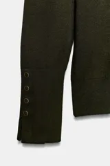 Jersey de punto liso en color beige, con cuello alto y manga larga con detalle de botones metálicos en los puños.