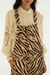 Jardinero largo confeccionado en denim con estampado animal print de cebra en tonos beige y marrón. Presenta tiradores regulables, cierre frontal con botones, bolsillos laterales y piernas amplias con ajuste en los tobillos.