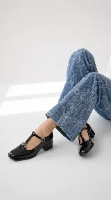 Zapatos de tacón bajo tipo Mary Jane con tira en T, confeccionados en charol color burdeos, con puntera cuadrada y cierre de hebilla lateral.