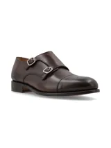 Zapato tipo Monk Strap de cuero color marrón oscuro, con doble hebilla metálica plateada y puntera reforzada.